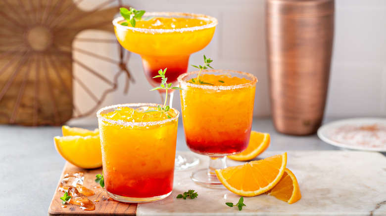 tequila sunrise cocktails on a cutting board with orange wedge garnish