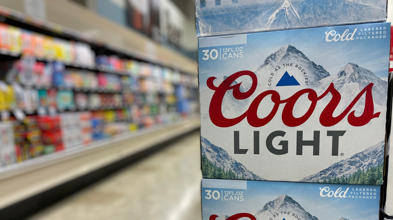 Display of Coors Light with beer section in grocery store blurred in background