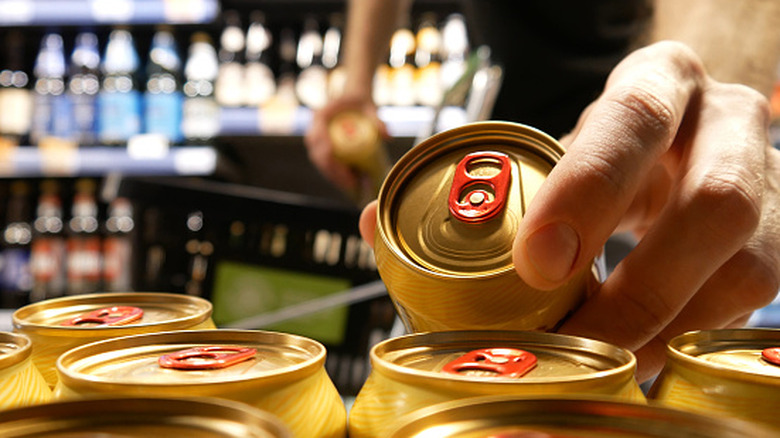 Hand picking up gold beer can off the shelf