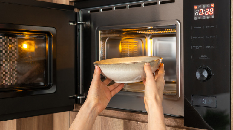 Hands placing a white bowl in microwave