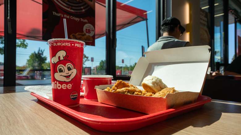 Chickenjoy fried chicken, biscuits, soda, and sides on a tray in a Jollibee restaurant