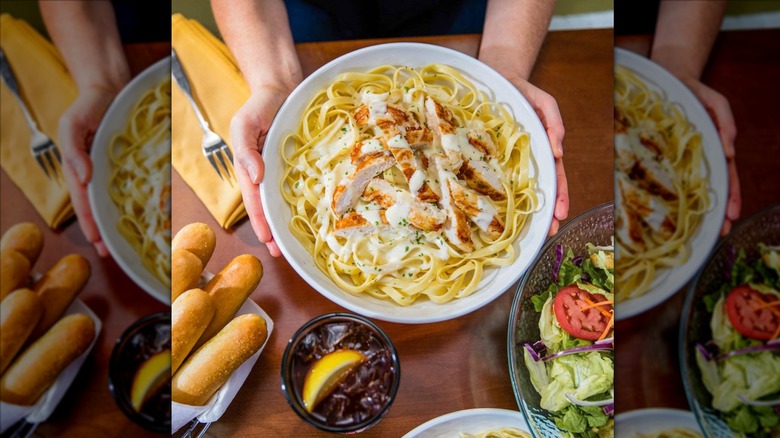 Hands holding bowl of Olive Garden chicken alfredo