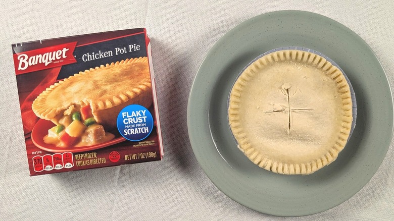 A pot pie on a plate next to a box for a Banquet chicken pot pie