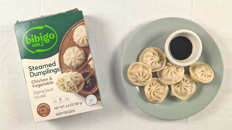 A plate of steamed dumplings with sauce next to a box of Bibigo dumplings