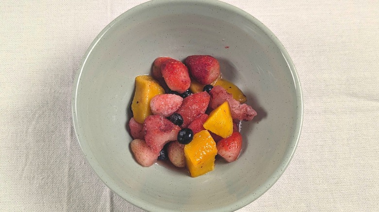 A close-up of a bowl of frozen strawberries, blueberries, and mango in a blue bowl