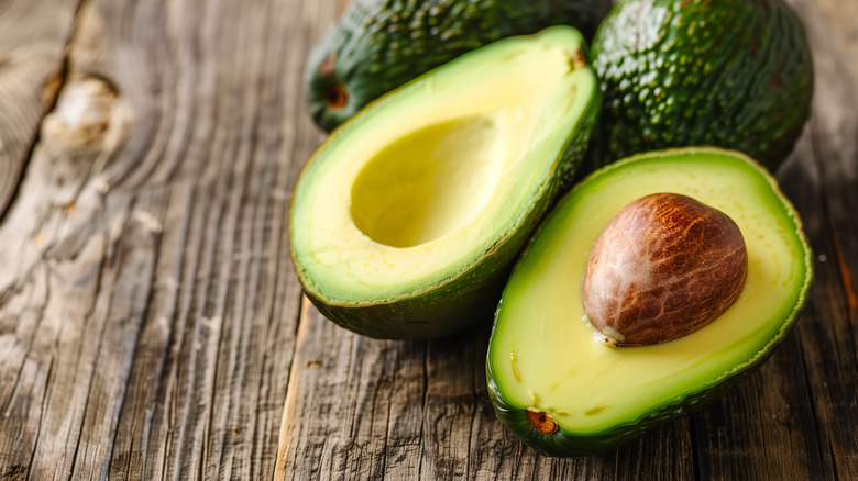 Halved avocado next to whole avocados on wooden background