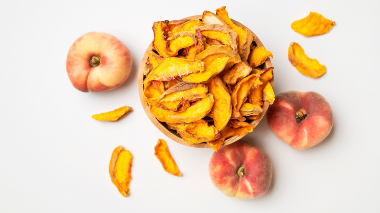Bowl of dried peach slices next to whole fresh peaches