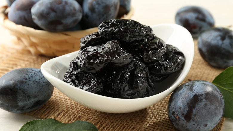 Bowl of prunes next to fresh plums