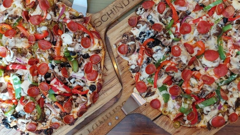 Two loaded whole pizzas on pizza peels at Schindy's