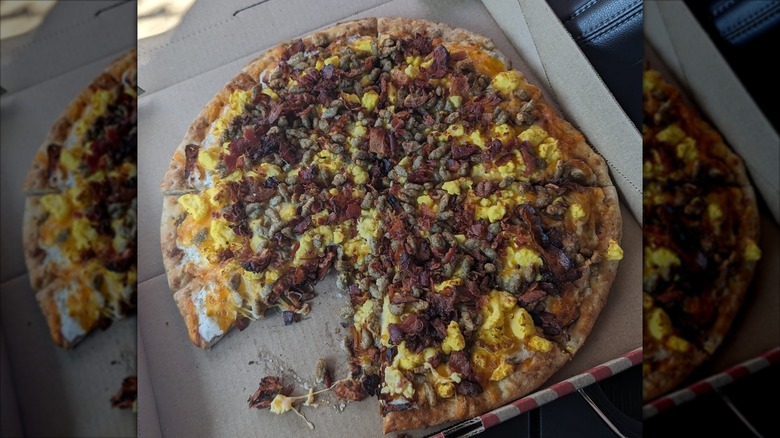 Whole QT breakfast pizza in box with one piece missing