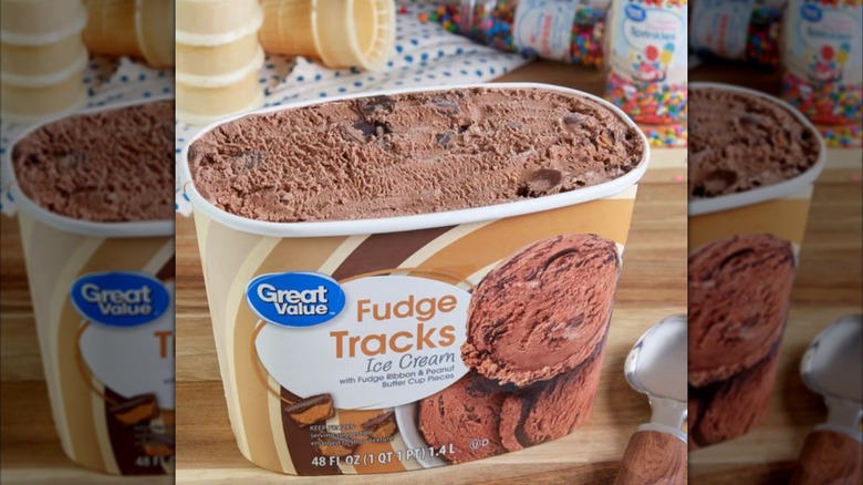 Half gallon of fudge tracks ice cream on table beside sprinkles and cones