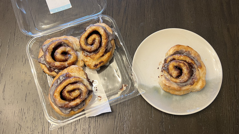 Fresh from Meijer glazed cinnamon buns in a plastic container and a whole one on a white plate