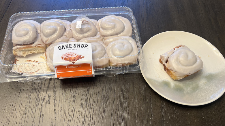 Aldi Bake Shop Bakery cinnamon rolls in a plastic container and a whole one on a white plate