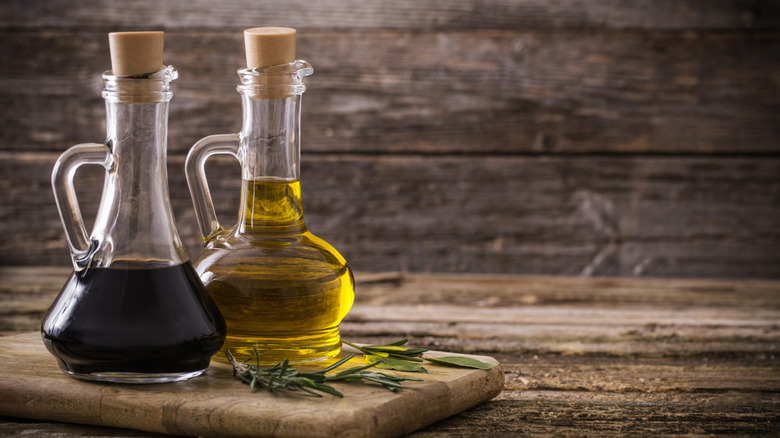 Glass bottles of oil and vinegar on wooden cutting board