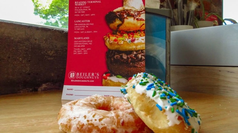 A sprinkled and glazed doughnut set in front of a flyer for Beiler's Doughnuts