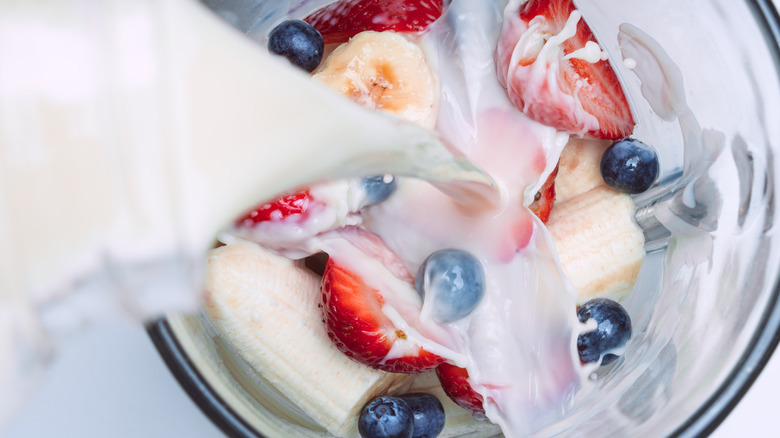 Milk being poured on top of fruit in a blender to make a smoothie