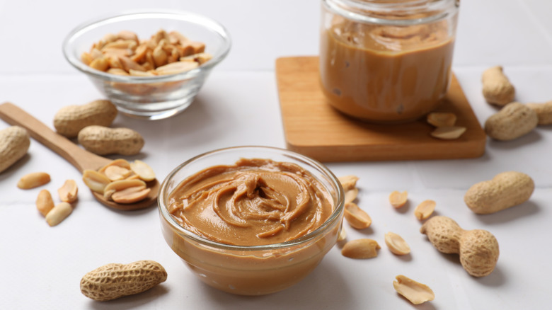 Peanut butter in glass dish, surrounded by whole peanuts