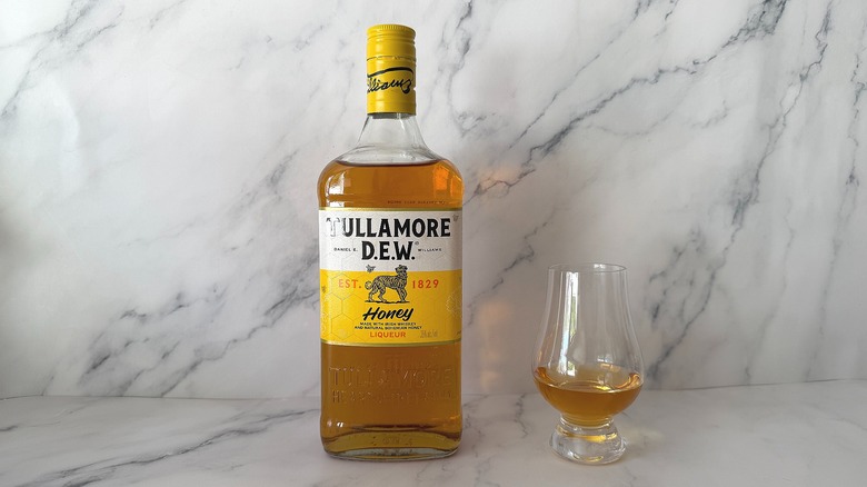 Bottle of Tullamore D.E.W. Honey next to the spirit in a glencairn glass on marble surface