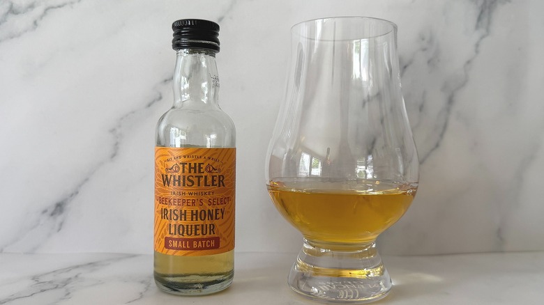 Bottle of The Whistler Honey next to the spirit in a glencairn glass on marble surface