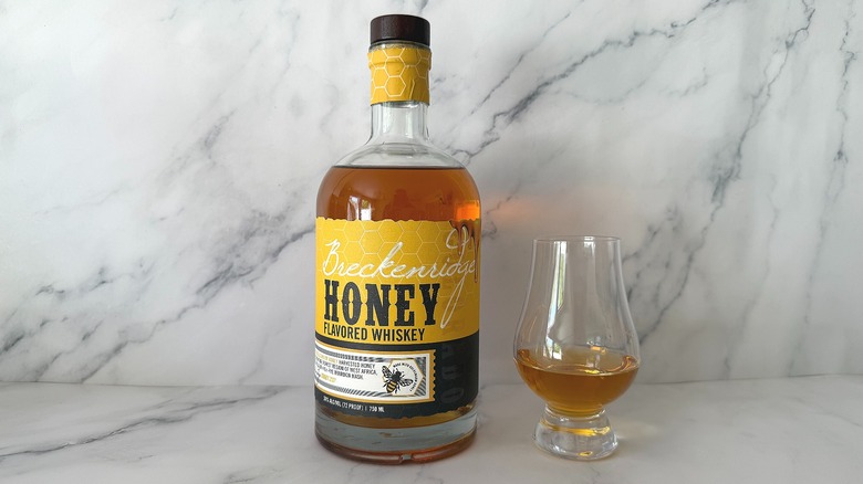 Bottle of Breckenridge Honey Flavored Whiskey next to the spirit in a glencairn glass on marble surface
