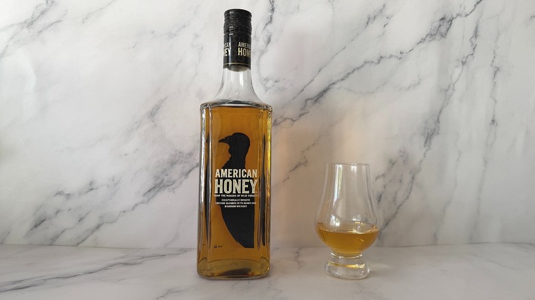 Bottle of American Honey next to the spirit in a glencairn glass on marble surface