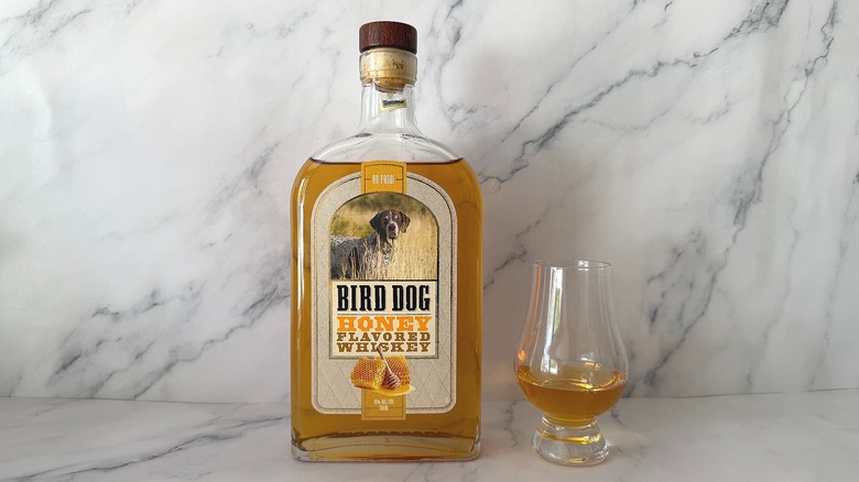 Bottle of Bird Dog Honey next to the spirit in a glencairn glass on marble surface