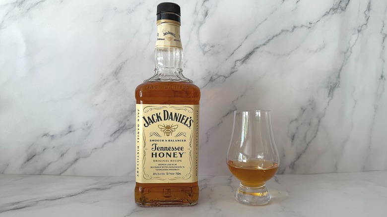 Bottle of Jack Daniel's Tennessee Honey next to the spirit in a glencairn glass on marble surface