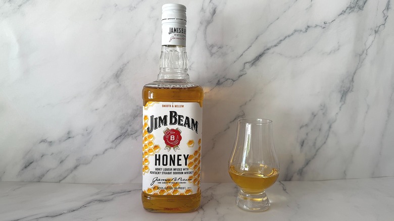 Bottle of Jim Beam Honey next to the spirit in a glencairn glass on marble surface