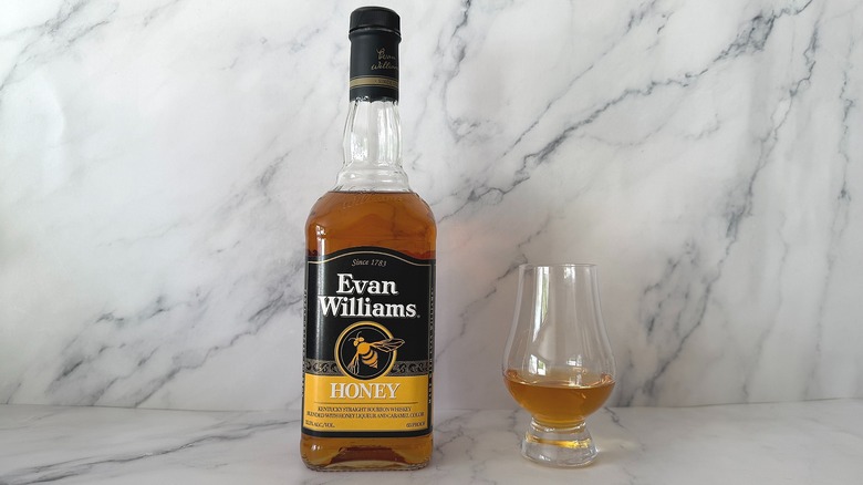 Bottle of Evan Williams Honey next to the spirit in a glencairn glass on marble surface