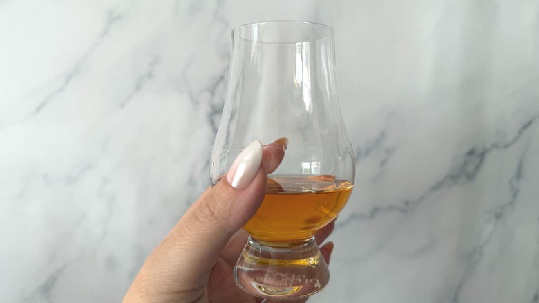 Hand holding glencairn of honey whiskey against marble background