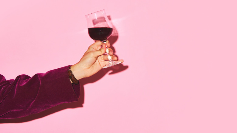 Hand holding a glass of red wine against a pink wall