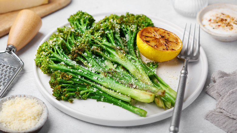 Cooked and seasoned broccolini on white plate with charred lemon