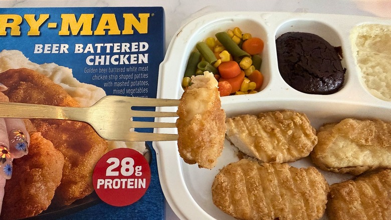 Fork holding piece of Hungry-Man beer battered chicken above meal and box