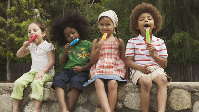 Four children sitting on a beach wall, enjoying ice cream with the forest in the background