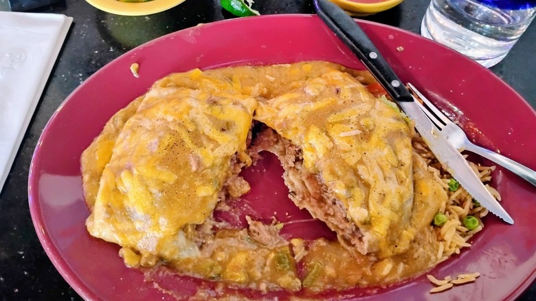 Mexican hamburger on a red plate: Burger patty cut in half, stuffed in a tortilla, drizzled with cheese and refried beans