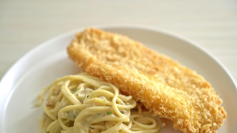 A close-up of a fried fish fillet served with spaghetti on a white plate