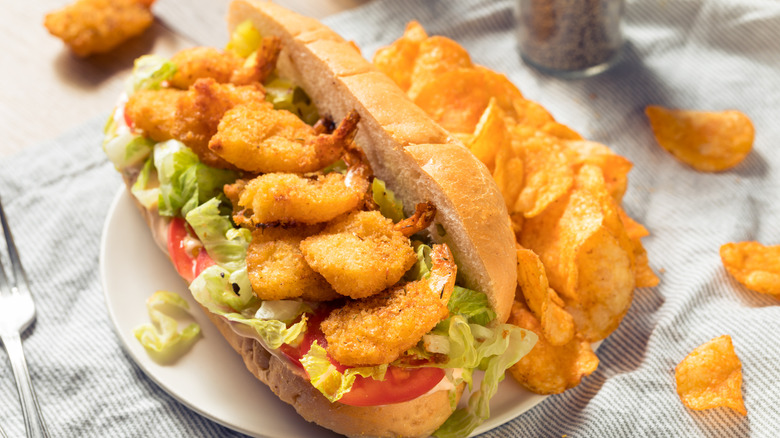 Shrimp Po Boy Sandwich with Lettuce and Tomato on white plate with potato chips