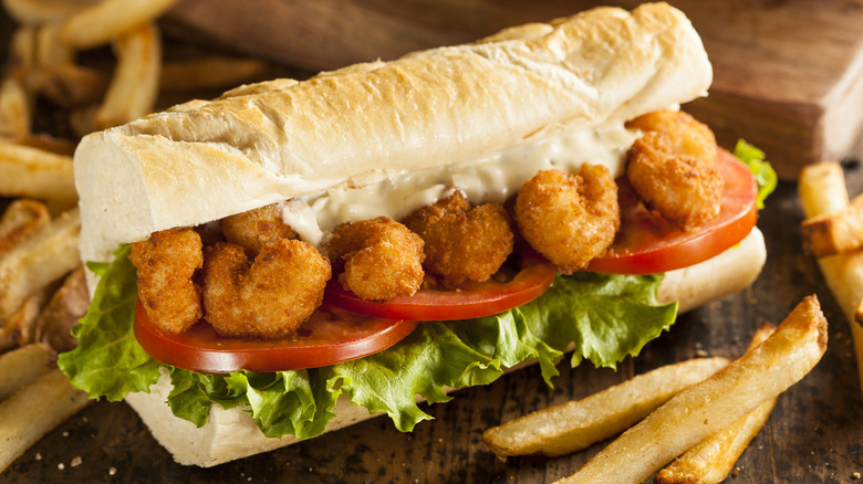 Homemade shrimp po'boy sandwich on brown board with french fries