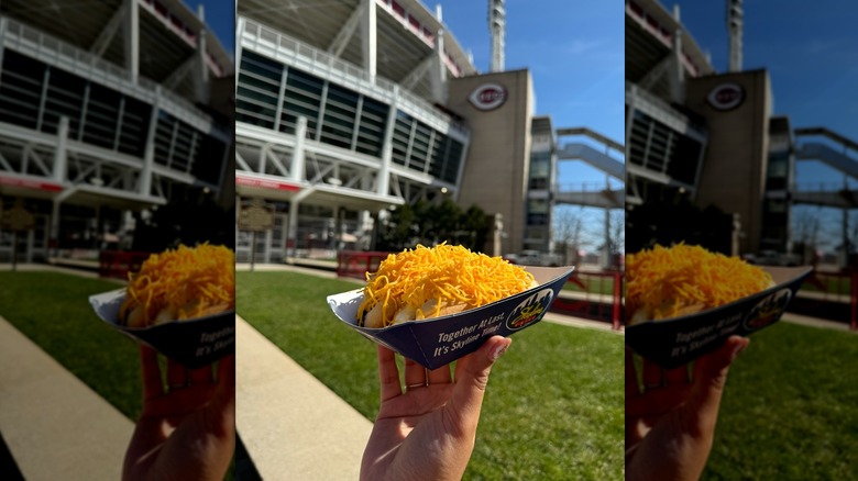 Hand holding a Skyline Chili Coney Dog in front of Cincinnati ballpark