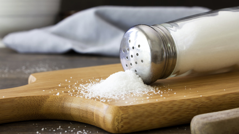 Salt spilling out of shaker onto wooden cutting board