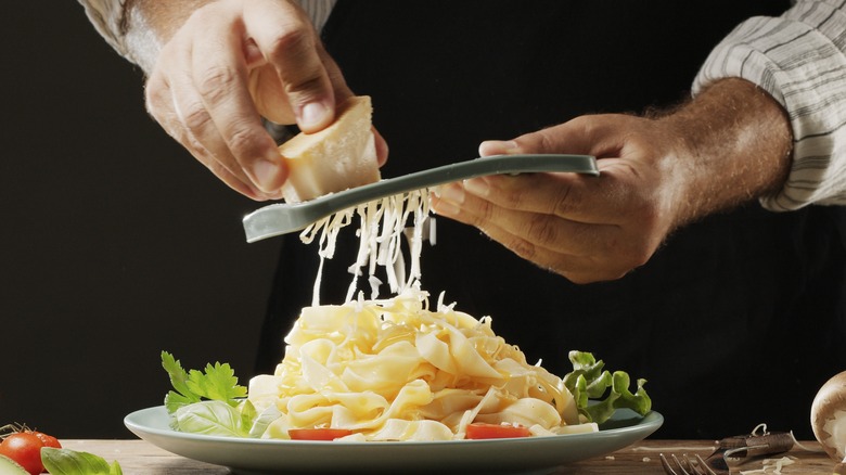 A person grating cheese over pasta