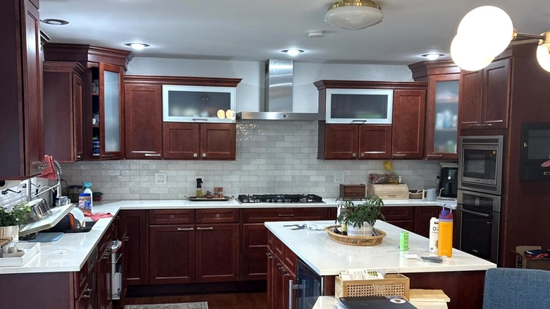 Kitchen with gray tile backsplash, dark cherry wood cabinets, and white counters