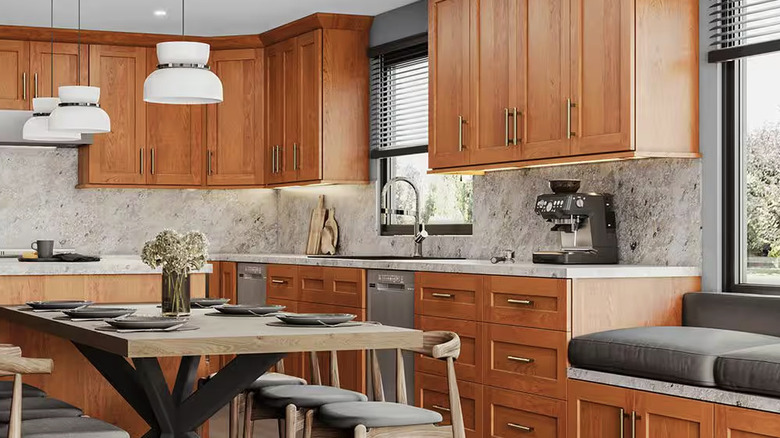 Kitchen with orange tinted wood cabinets, white granite counters, and gray table lined with chairs