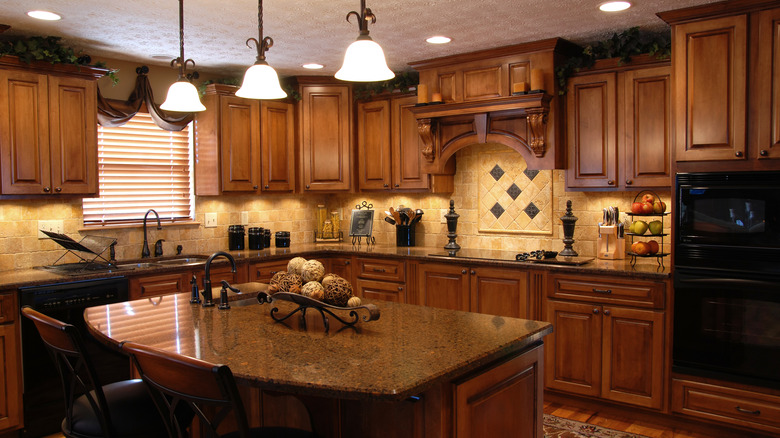 Rustic style kitchen with wood cabinets, hanging lamps, granite island, and tile walls