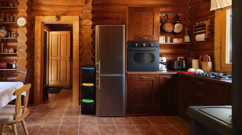Kitchen with warm wood cabinets and walls, steel fridge, black oven, and brown tile flooring