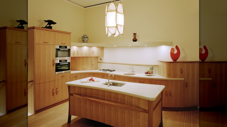 Kitchen with off white walls and wood cabinets, curved counter and island, decorated with vases and sculptures
