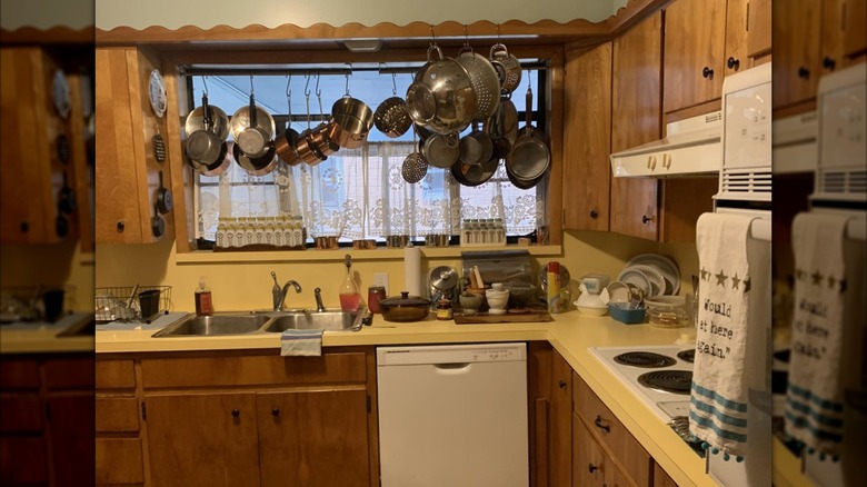 Kitchen with wood cabinets and yellow laminate countertop with pots and pans hanging down in front of window