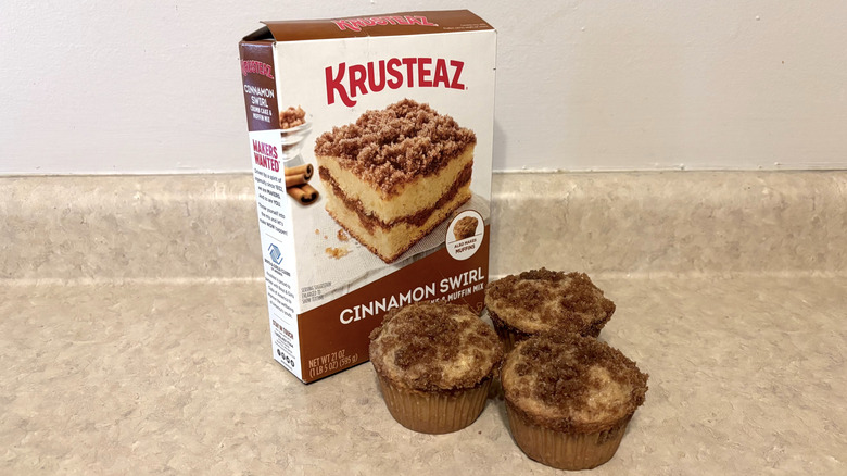 Krusteaz cinnamon swirl muffin mix box with muffins on neutral counter