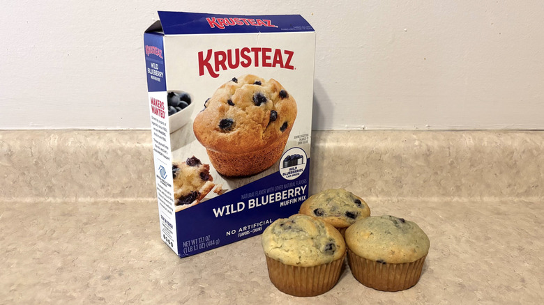 Krusteaz wild blueberry muffin mix box with muffins on neutral counter
