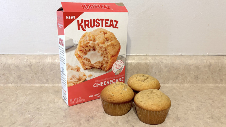 Krusteaz cheesecake muffin mix box with muffins on neutral counter